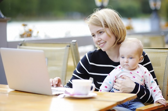 femeie-care-zambeste-si-sta-cu-bebelusul-in-brate-in-fata-laptopului