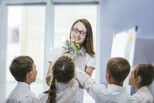 grup-de-elevi-din-clasele-primare-incercand-sa-i-ofere-un-buchet-de-flori-galbene-doamnei-invatatoare