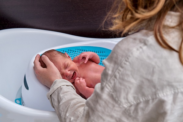 dispozitiv de imbaiere pentru bebelusi mama care isi mangaie pe cap bebelusul ce plange la imbaiere