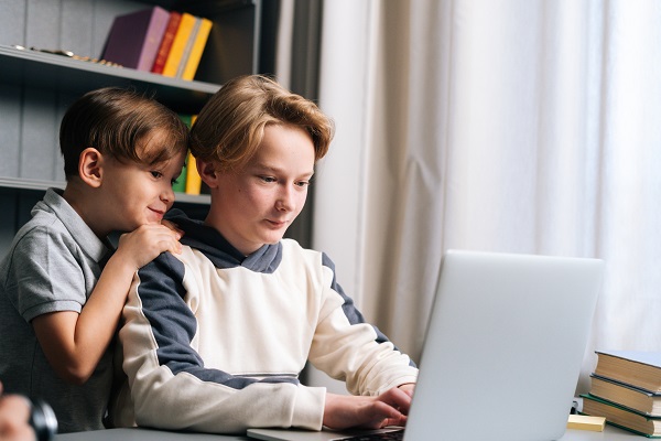 baietel zambitor uitandu-se cu atentie la un adolescent care foloseste laptop-ul