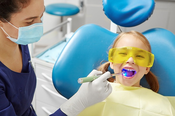 fetita stand pe scaun la dentist si avand ochelari de protectie intrucat medicul îi face un tratament de sigilare a dintilor