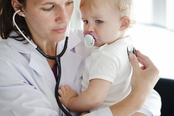 doctorita care tine in brate un bebelus ca sa-l poata asculta cu stetoscopul