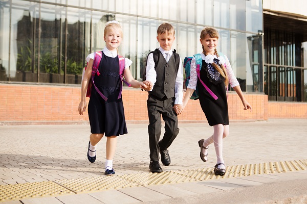 trei elevi de clasele primare in uniforma plecand din curtea scolii