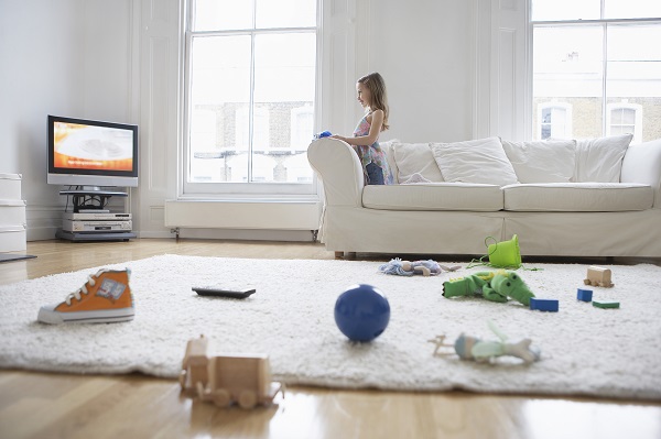 fetita care se uita la televizor in timp ce jucariile sunt imprastiate pe jos