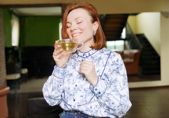 femeie care este cuprinsa de o stare de bine in timp ce savureaza un ceai