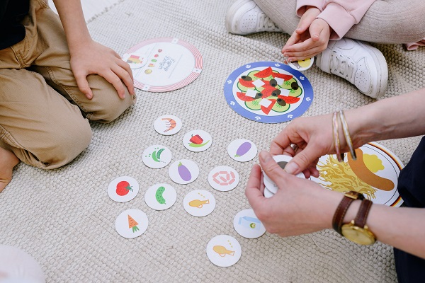 femeie adulta care se joaca cu cartonase cu diverse obiecte cu doi copii