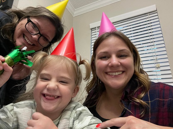 doua femei si o fetita, vesele si purtand pe cap coifuri colorate pentru petrecere