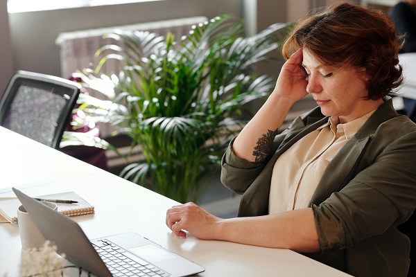 femeie care se afla la birou, in fata laptop-ului si se confrunta cu o durere de cap