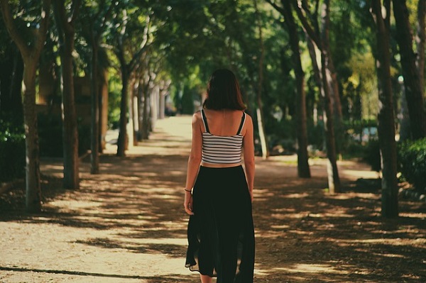 femeie cu bluza cu spatele gol si fusta neagra plimbandu-se la umbra copacilor