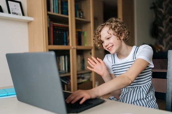 adolescenta cu parul scurt, cret, care îi face cu mana cuiva cu care sta de vorba online, pe laptop