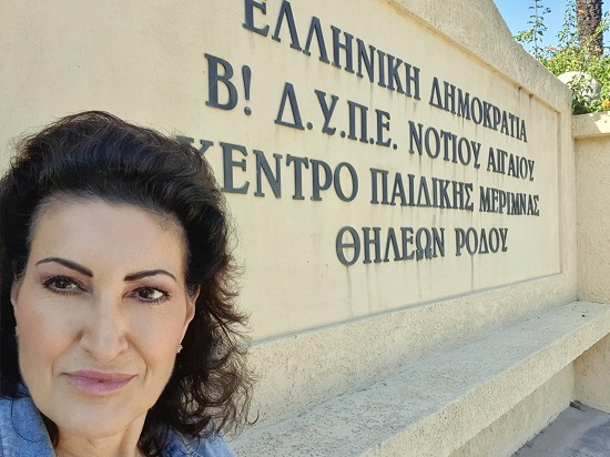 femeie care sta cu spatele la un zid pe care scrie in limba greaca