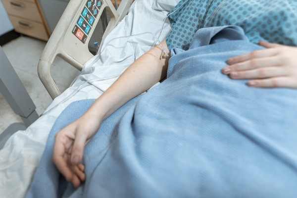 femeie aflata pe patul de spital cu perfuzie si fiind invelita cu o patura albastru deschis