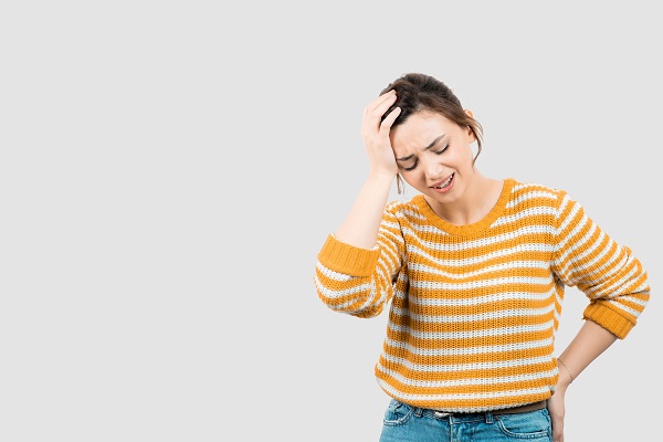 femeie tanara, in pulover si blugi, ce se confrunta cu dureri de cap si de spate