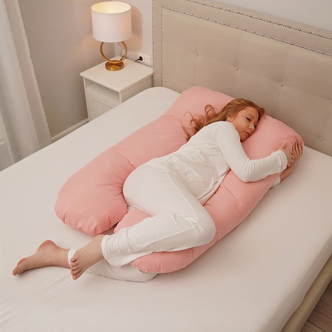 femeie insarcinata in pijama alba dormind pe o perna roz pentru gravide