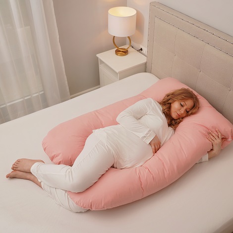 femeie insarcinata in pijama alba dormind pe o parte pe o perna roz pentru gravide 