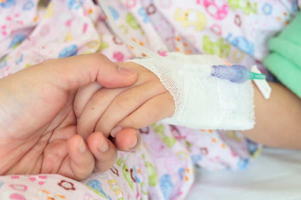 mana de femeie care tine de mana o fetita careia i se face tratament cu perfuzii