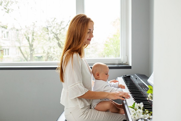 mama care isi tine bebelusul pe genunchi in timp ce canta la pian