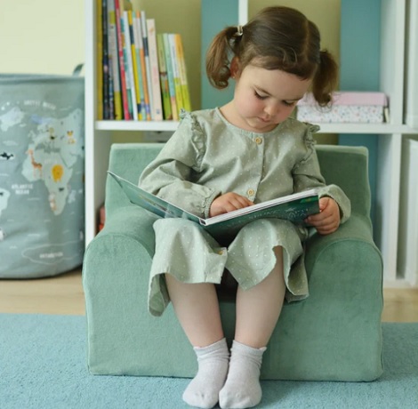 fetita care sta si citeste pe un fotoliu pentru copii vernil