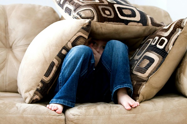 copil care se ascunde intre perne pe o canapea
