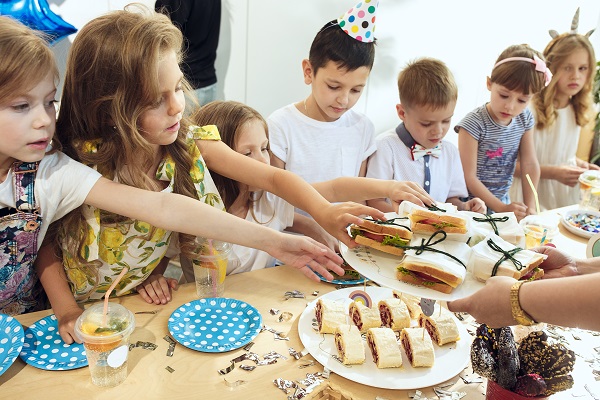 copii aflati la o petrecere care se pregatesc sa se serveasca cu sandvisuri la masa
