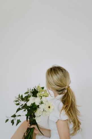 femeie blona cu o coada de cal eleganta la spate si un buchet de flori in mana