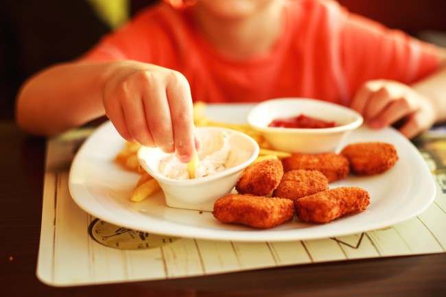 copil care mananca mancare tip fast food, cartofi prajiti si nuggets de pui