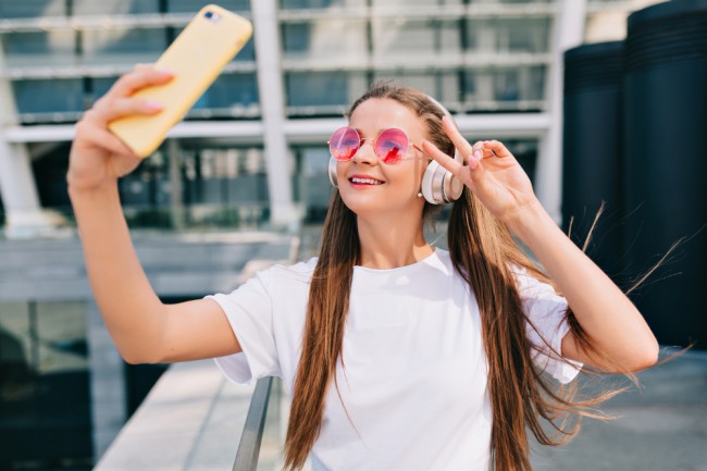 adolescenta cu ochelari de soare si casti care se filmeaza cu telefonul mobil