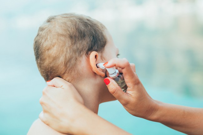 femeie care desfunda urechea unui baietel cu spray auricular