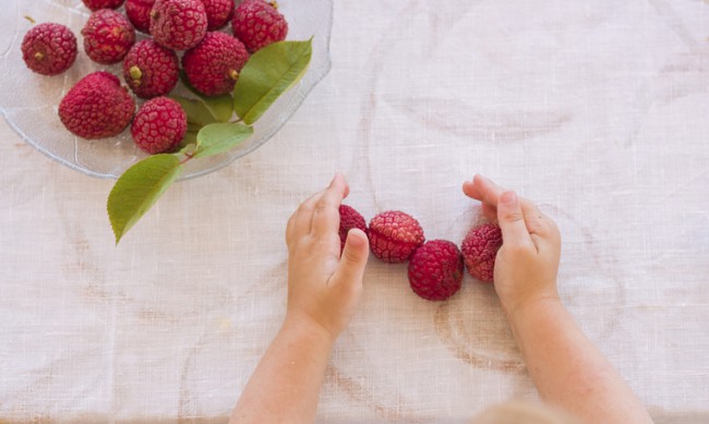 doua maini de copil si fructe de litchi pe masa