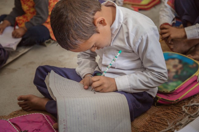 Copil concentrat de școală rurală care studiază pe podea și scrie în caiet