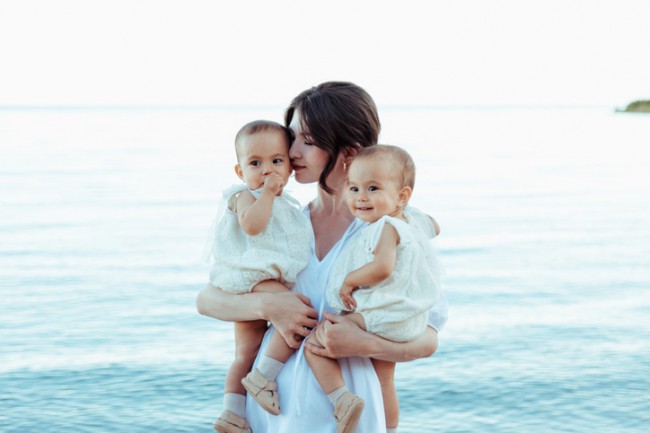 Mama care ține în brațe fiice gemene pe plajă