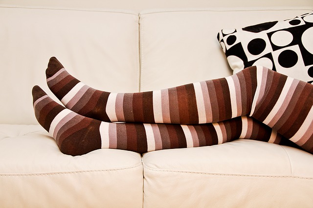 imagine cu picioarele unei femei lungita pe o canapea crem, incaltata cu ciorapi colorati