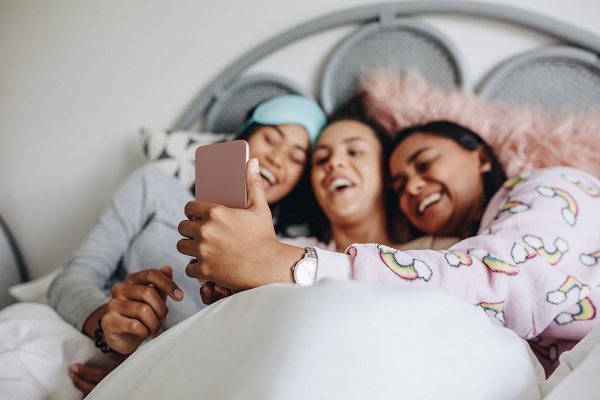 trei fete in pat rad si se uita pe telefon
