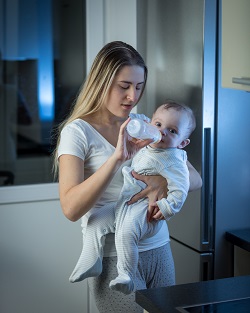 Mama ce isi tine bebelusul in brate, in pozitie verticala, ca sa ii dea lapte cu biberonul