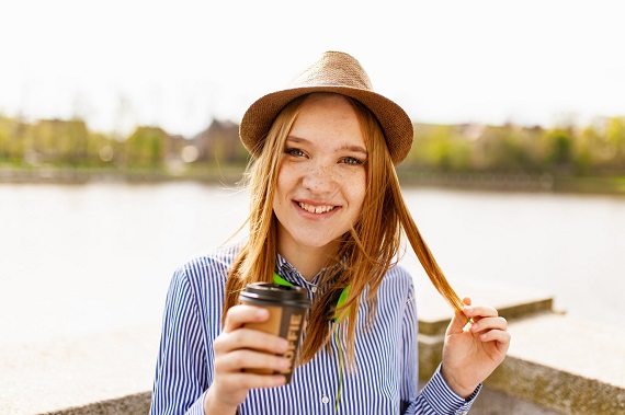 Fata binedispusa cu palarie, care tine in mana un pahar cu cafea