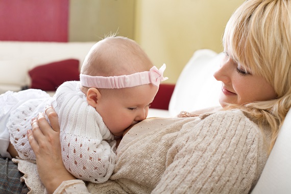 Mama ce isi alapteaza bebelusul stand in pat, rezemata de o perna