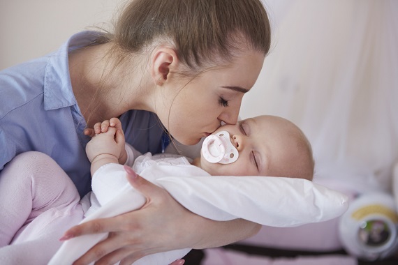 Mama ce isi saruta pe obrajor bebelusul, ce are o suzeta