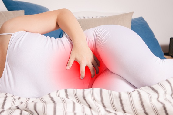 Femeie intinsa pe pat, care are dureri in partea inferioara a abdomenului