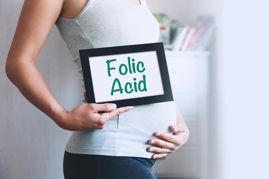 Femeie insarcinata ce tine in mana o rama in care se afla o pagina pe care scrie Acid Folic