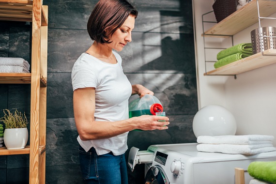 Femeie ce masoara cantitatea de detergent pe care o va introduce in masina de spalat