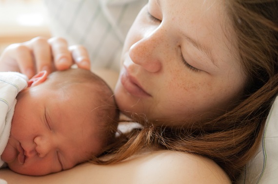 Mama ce isi mangaie pe cap bebelusul care doarme pe pieptul ei