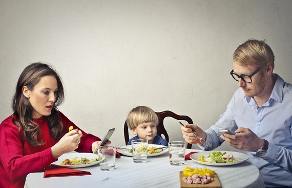 Familie la masa, mama si tatal stand cu ochii in telefon