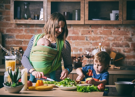 Mama cu bebelus si cu celalalt copil mai mare, gatind legume cu frunze verzi