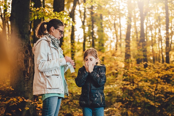 Mama si fiica intr-o padure, toamna, iar fiica are probleme din cauza nasului care curge 