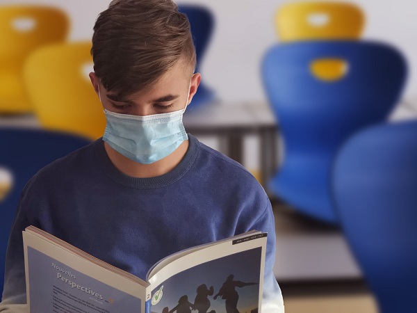 Adolescent purtand masca de protectie in clasa in timp ce citeste dintr-o carte