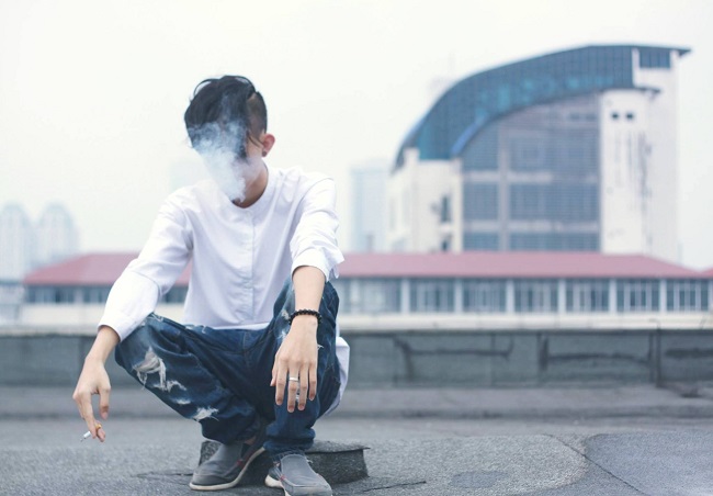 Adolescent care sta singur pe un acoperis si are fata invaluita in fum de tigara