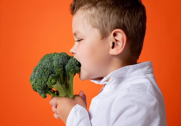 Baietel in camasa care a inchis ochii si musca dintr-un broccoli