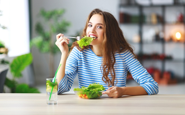 Femeie tanara care mananca o salata verde cu rosii