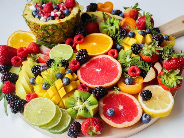 Diverse fructe pe un platou de lemn: kiwi, grapefruit, portocal, capsune, mure, afine si altele