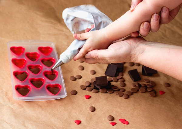 mana-de-copil-ce-este-sprijinita-de-mana-unei-femei-pentru-a-putea-manipula-dispozitivul-de-decorare-ca-sa-toarne-un-amestec-de-ciocolata-in-forme-de-inima